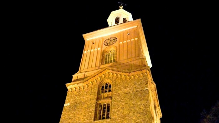 Der Turm einer Kirche ist beleuchtet und hebt sich vor dem dunklen Himmel ab