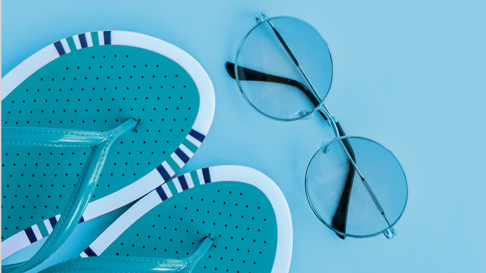 Helle blaue Sonnenbrille und passende gemusterte Bademütze vor einem hellblauen Hintergrund.