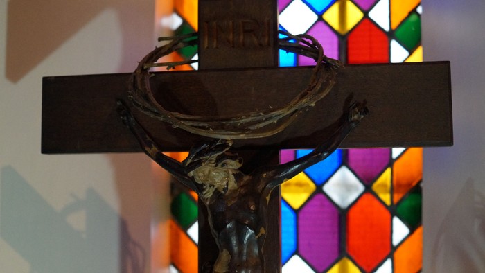 Ein Kruzifix vor einem bunt gefärbten Fenster.