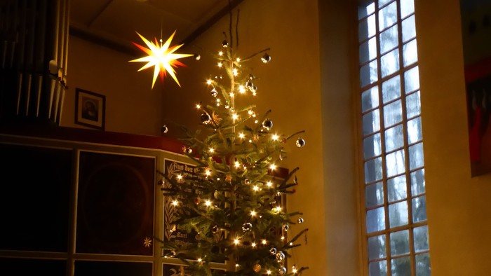 Ein wunderschön geschmückter Weihnachtsbaum leuchtet hell in einem gemütlichen, schwach beleuchteten Raum mit warmen Lichterketten der Feiertage.