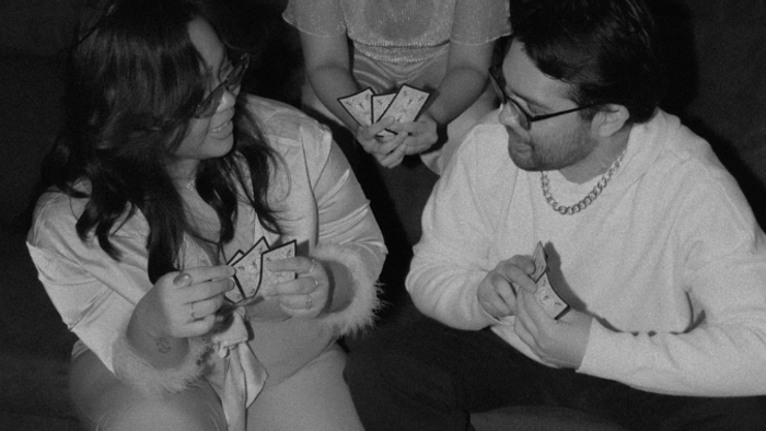 Eine Gruppe, die mit konzentrierten Gesichtern Karten spielt und Spielkarten sowie kleine Spielzeuge in den Händen hält.