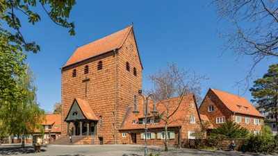 Ein rotes Backsteingebäude mit einem hohen Turm und kleineren Nebengebäuden unter einem klaren blauen Himmel.