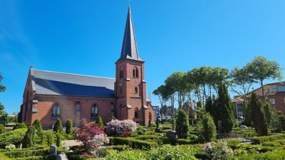 En rød murstenskirke med spir med omgivelser og blomsterbænke