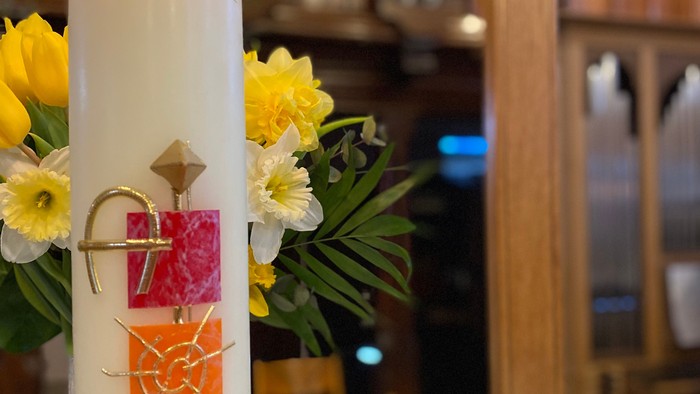 Kerze mit buntem Kreuz und Blumen neben einem offenen Buch