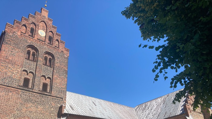 Gammel teglkirke med tårn og klokke under klar blå himmel