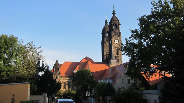 Ein Auto parkt vor einer Kirche mit hohem Turm und rotem Dach.