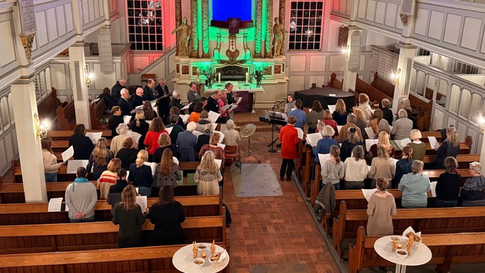 Ein überfüllter Kircheninnenraum mit Besuchern, die während eines Abendgottesdienstes in den Bänken sitzen, beleuchtet von farbenfroher Bühnenbeleuchtung.