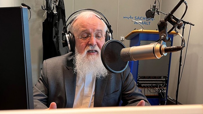 Ein älterer Mann mit Bart nimmt einen Podcast oder eine Radiosendung mit professioneller Studioausrüstung auf.