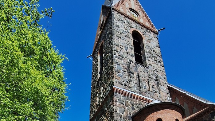 Gruppe von Menschen vor alter Kirche mit hohem Turm und blauen Himmel