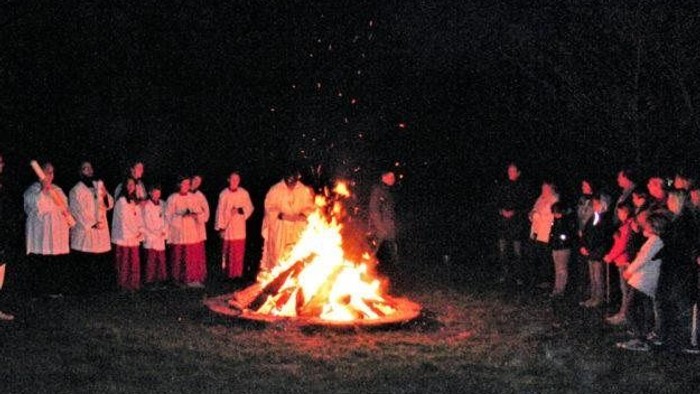 Gruppe versammelt sich um ein nächtliches Lagerfeuer auf einer grasbewachsenen Freifläche, teilt Wärme und Gespräche.