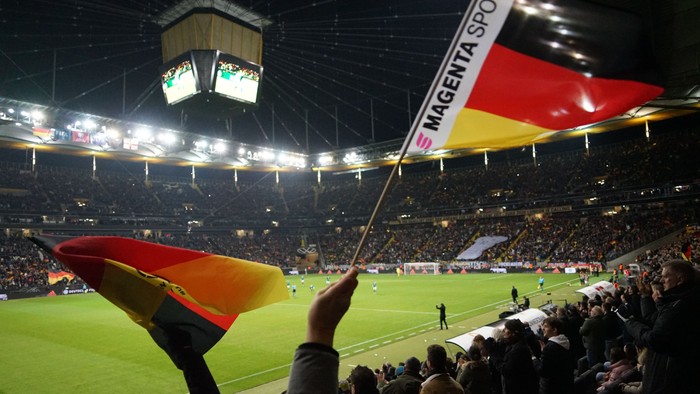 Zuschauer winkt mit einer deutschen Flagge in einem lebhaften, gut besuchten Fußballstadion während eines Spiels.