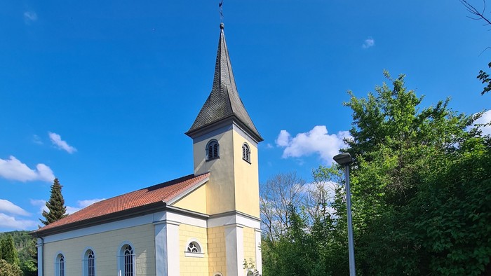 Idyllische Kirche mit hohem Kirchturm in einer üppigen, grünen Landschaft an einem sonnigen Tag.