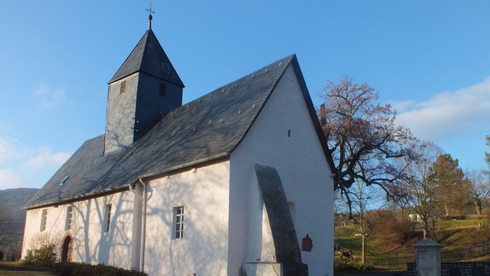 Idyllische weiße Kirche mit steilem Dach und Glockenturm in einer ruhigen, grasbewachsenen Landschaft.