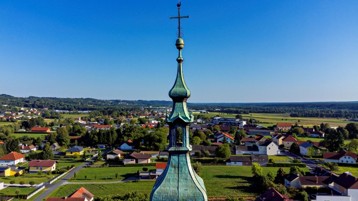Luftaufnahme eines malerischen Dorfes mit einem markanten Kirchturm und weitläufiger grüner Landschaft.