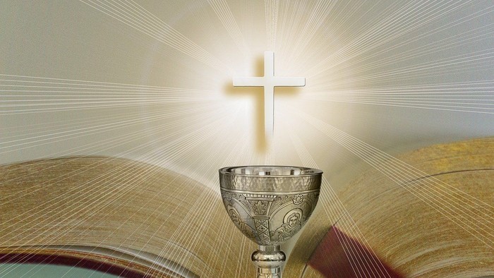Ein silberner Kelch vor einem aufgeschlagenen Buch mit einem leuchtenden Kreuz darüber