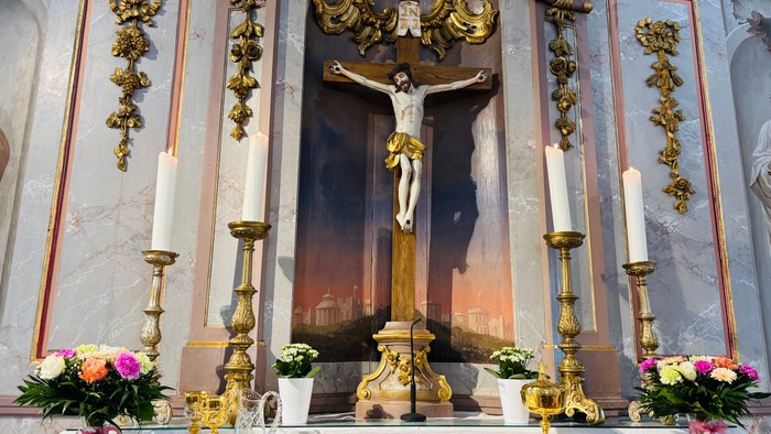 Aufwendiger Altar mit einem Kruzifix, verziert mit prunkvollen goldenen Verzierungen, Kerzen und Blumengestecken.