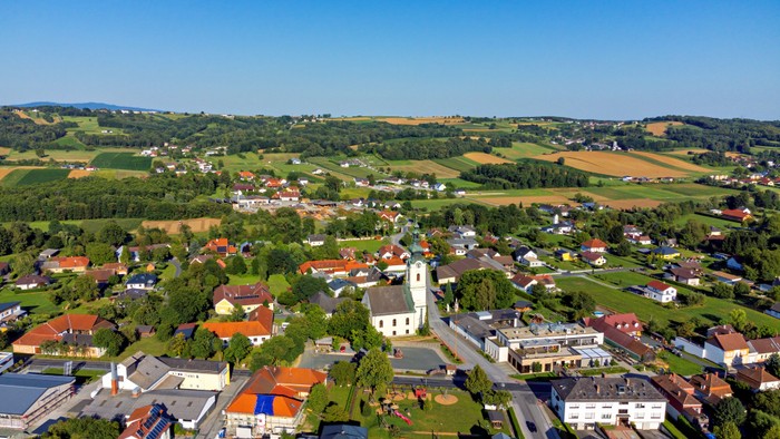 Luftaufnahme eines idyllischen ländlichen Dorfes, umgeben von saftig grünen Feldern und sanften Hügeln.
