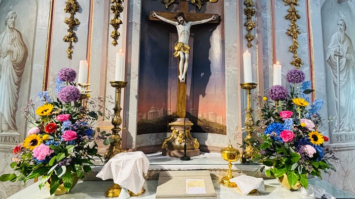 Aufwendiger Altar mit einer Kreuzigungsszene, verziert mit farbenfrohen Blumengestecken und Kerzenhaltern.