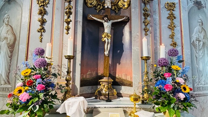 Aufwendiger Altar mit einer Kreuzigungsszene, verziert mit farbenfrohen Blumengestecken und Kerzenhaltern.