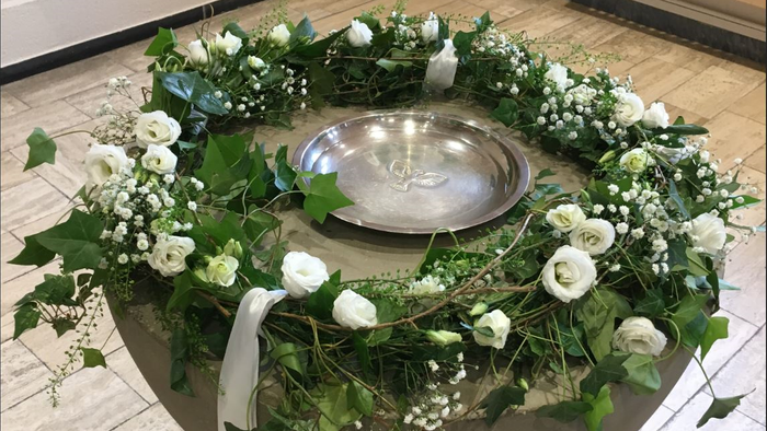 Ein runder Tisch mit weißen Blumen und grünem Laub, darauf eine silberne Schale