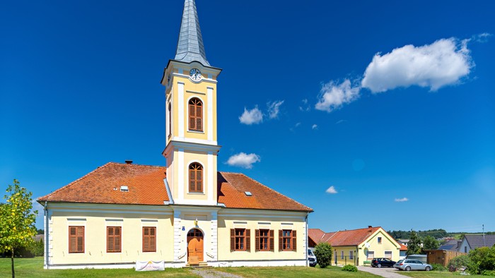 Eine charmante Kirche mit hohem Turm und rotem Ziegeldach vor einem klaren blauen Himmel.