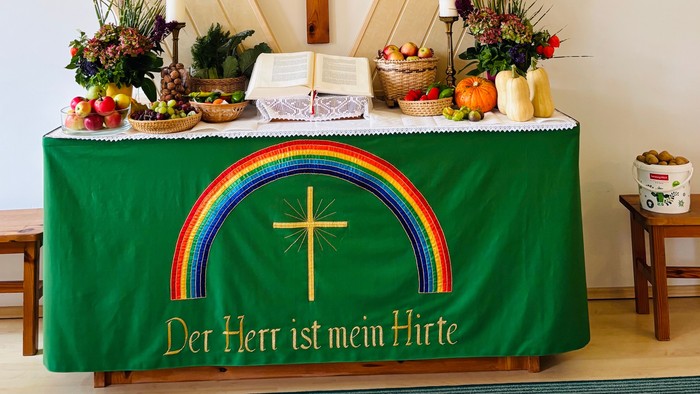 Verzierter Altartisch mit religiösen Symbolen, Früchten und dem Spruch *„Der Herr ist mein Hirte“* unter einem Regenbogenkreuz.