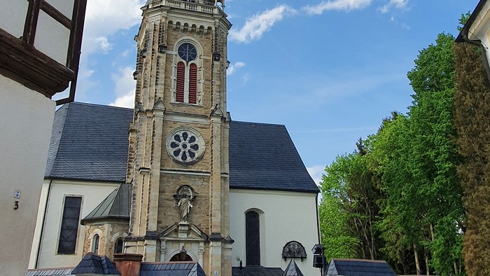 Kirchturm mit Uhr und Kreuzigungsgruppe vor weißem Gebäude