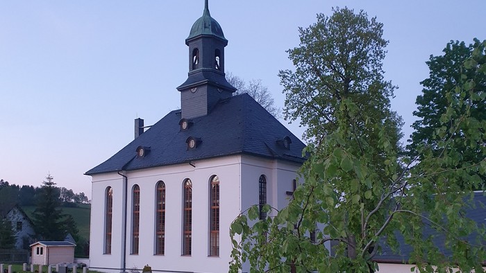 Kirche mit Friedhof und Bäumen im Hintergrund