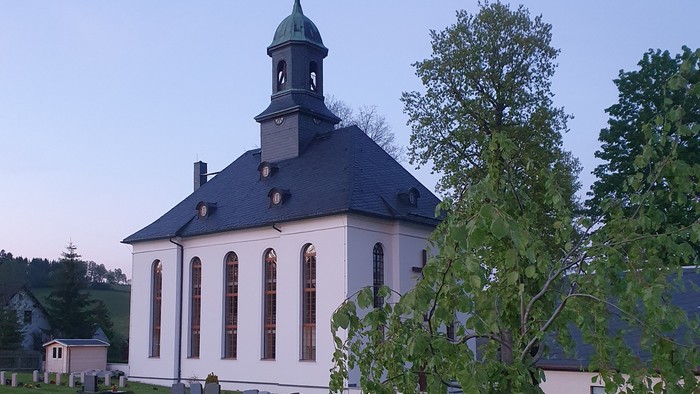 Kirche mit Friedhof und Bäumen im Hintergrund