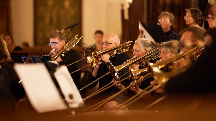 Eine Gruppe von Musiker:innen, die in einem Konzert Blechblasinstrumente spielen und sich konzentriert auf ihren Auftritt fokussieren.