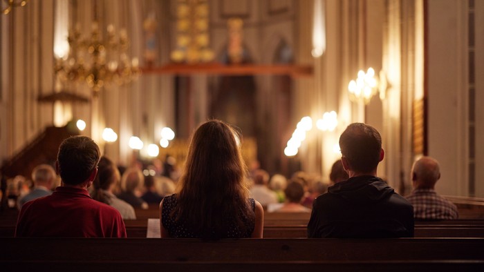 Ein ruhiger Gottesdienst mit Gläubigen, die zum Altar gewandt sind, beleuchtet von warmem Kerzenlicht und Kronleuchtern.