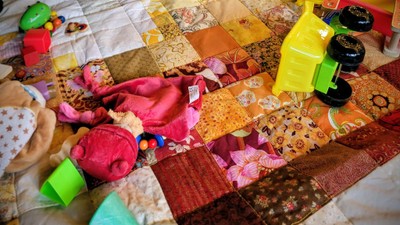 Bunte Stoffstücke und Stoffreste, zwischen denen verschiedene Spielzeuge und Nähutensilien auf einem Bett verstreut liegen.