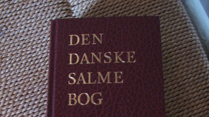 En mørkerød dansk salmebog med titlen *Den Danske Salmebog* af S. R. Kirke.