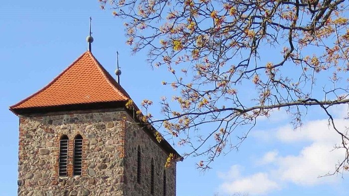 Steinige Kirche mit hohem Turm und rotem Dach unter blauem Himmel