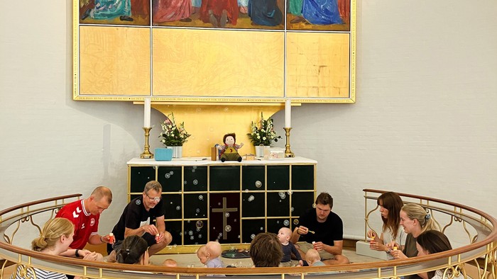 En gruppe af mennesker sidder i en halvcirkel om en altertavle i en kirke.