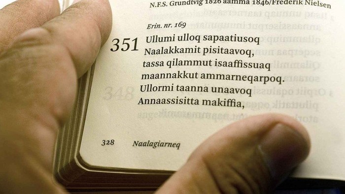 Hånd holder en åben bog med latin tekst og arabiske tal.