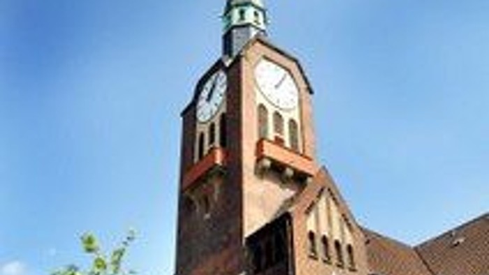 Eine markante Backsteinkirche mit hohem Kirchturm und Uhrturm vor einem klaren blauen Himmel.