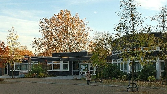 Moderne Campusgebäude, umgeben von herbstlichem Laub und einem offenen gepflasterten Innenhof.