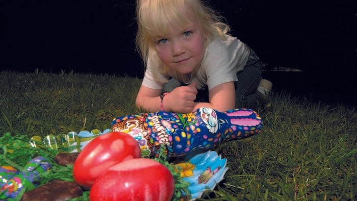 Ein junges Mädchen liegt im Gras neben bunt verpackten Spielzeugen und zwei roten Tomaten.