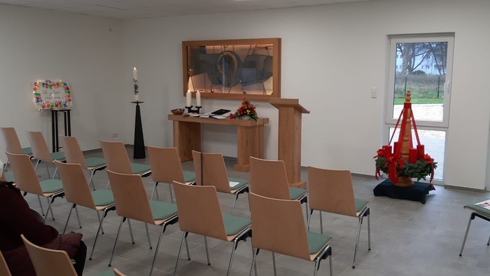 Ein ruhiger Raum mit Stühlen, die für eine Veranstaltung angeordnet sind, mit einem geschmückten Altar und einem blumigen Mittelstück.