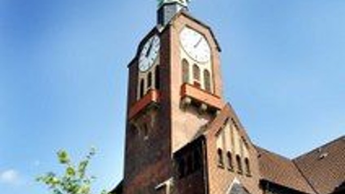 Eine markante Backsteinkirche mit hohem Kirchturm und Uhrturm vor einem klaren blauen Himmel.