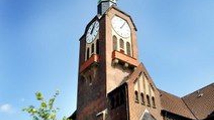 Eine markante Backsteinkirche mit hohem Kirchturm und Uhrturm vor einem klaren blauen Himmel.