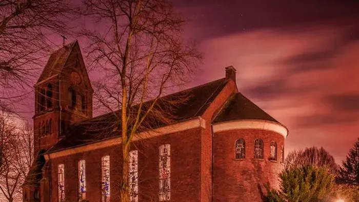Ein ruhiger Abendblick auf eine rote Backsteinkirche, die vor einem dramatischen Dämmerungshimmel erleuchtet ist.