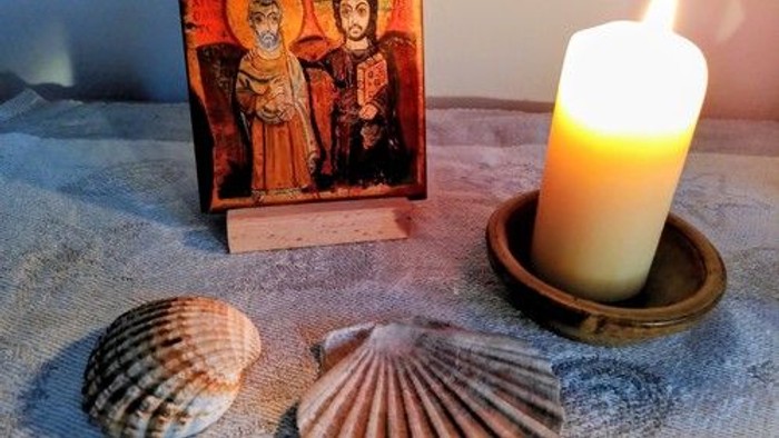 Religiöses Symbol, Muscheln und eine brennende Kerze auf einer strukturierten Oberfläche.