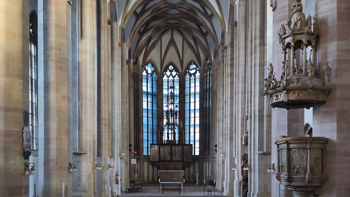 Große gotische Kathedrale im Inneren mit hohen Bögen, bunten Glasfenstern und hölzernen Kirchenbänken, die zum Altar führen.