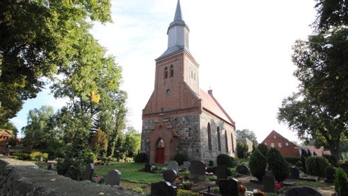 Idyllische Kirche mit hohem Turm, umgeben von einem ruhigen, gepflegten Friedhof.