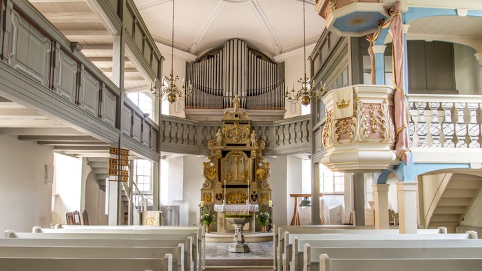 Historisches Kircheninneres mit prunkvollem Altar, Kirchenbänken und einer großen Orgel unter einem verzierten Balkon.