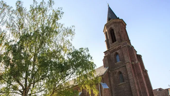Historische Backsteinkirche mit hohem Turm, umgeben von üppigem Grün unter klarem Himmel.