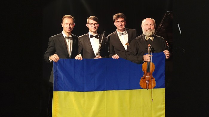 Vier Musiker halten eine ukrainische Fahne. Einer hält zudem eine Klarinette und ein anderer eine Geige.