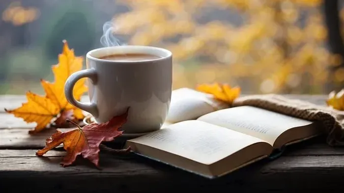 En hvid tekop i en bønnerod med damp, en åben bog og gule løver på en træbænke